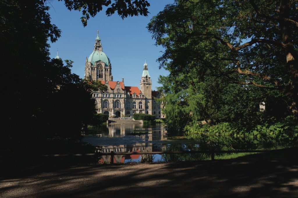 The New Town Hall in Hannover framed by lush trees and reflected in a serene lake.